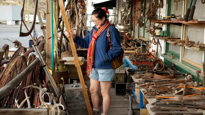 Person checking out vintage tools in an outdoor undercover section of a thrift store or scrap yard