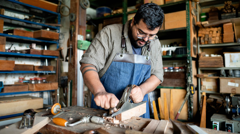 A carpenter using an antique plane on a piece of wood in his workshop