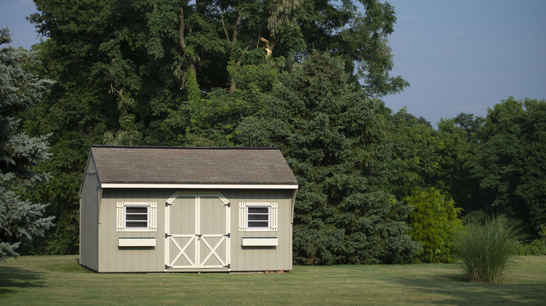 A neat shed in a manicured back yard with large trees behind it
