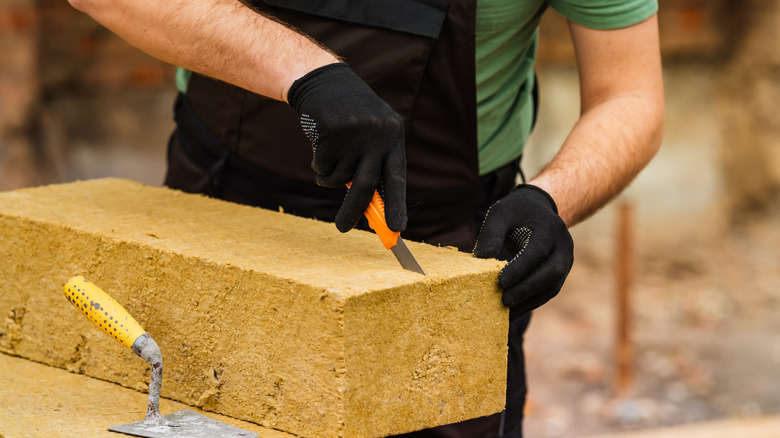 person cutting into a batt of mineral wool insulation with Xacto knife
