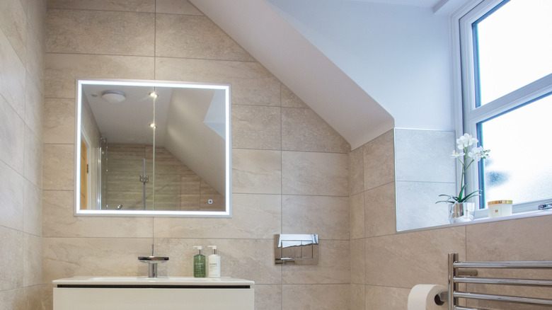 A bright neutral modern bathroom with tiled walls and a slanted ceiling
