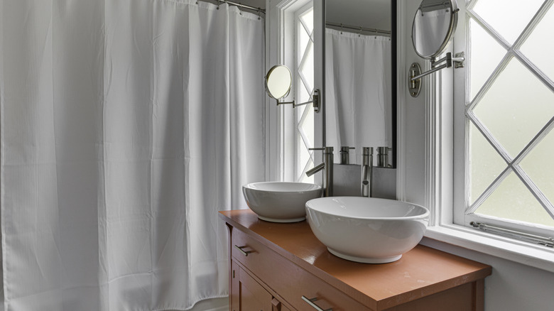 A modern clean bathroom with a white shower curtain on a tub and two white sinks