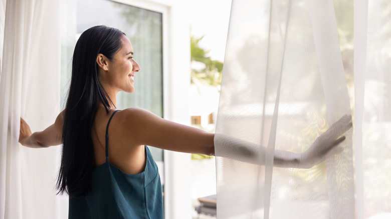 A woman in front of opened doors with sheer curtains.