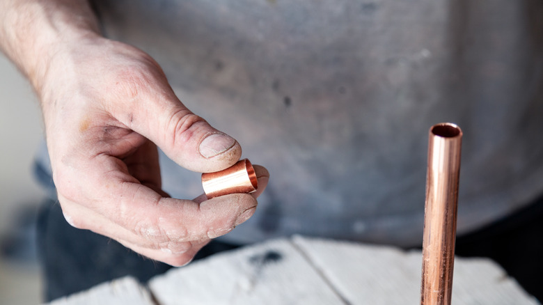 Man holding copper end cap near a copper pipe