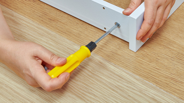 A person's hands assembling furniture with a basic screwdriver.