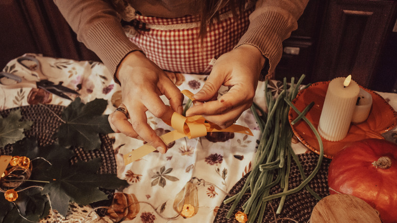 A pair of hands making fall decor with ribbons, faux foliage, and other craft supplies.