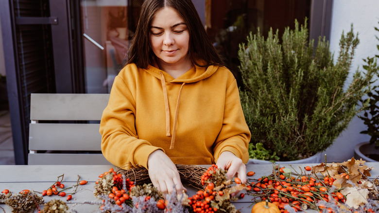 A woman putting orange berries and dried greenery around a wreath of brown twigs.