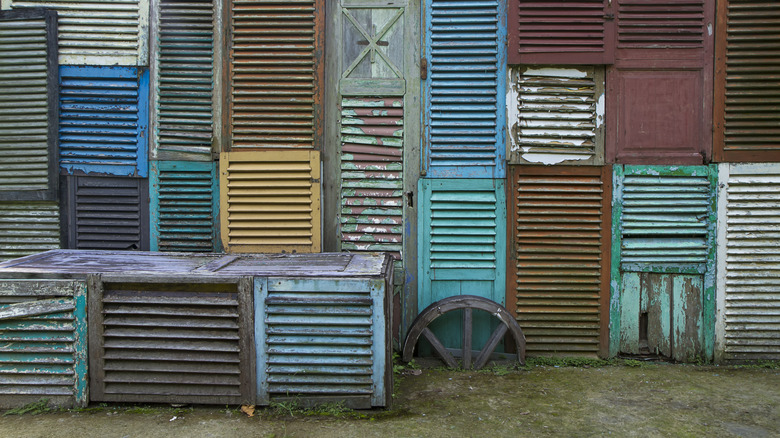 Multiple old shutters in various colors on display at a reclamation yard.
