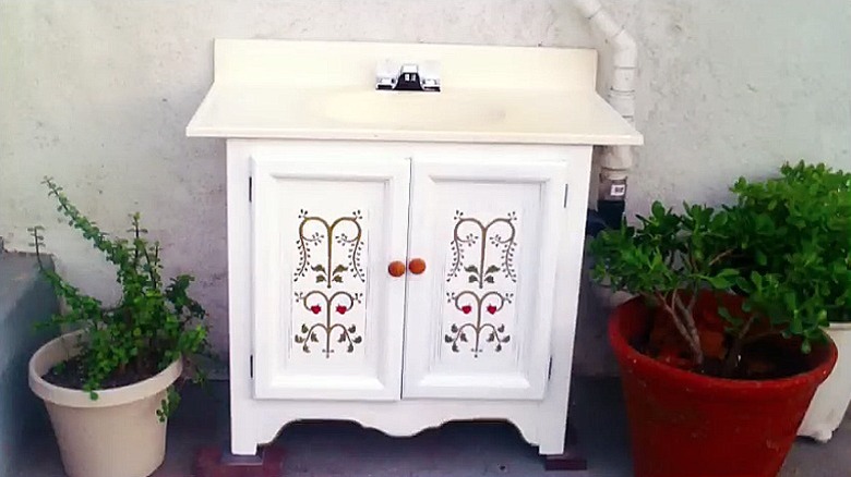 A white vintage style vanity made using an old cabinet with a pretty painted design on the front
