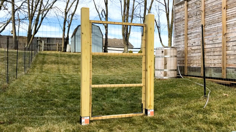 A wooden gate on a wire fence around a property.