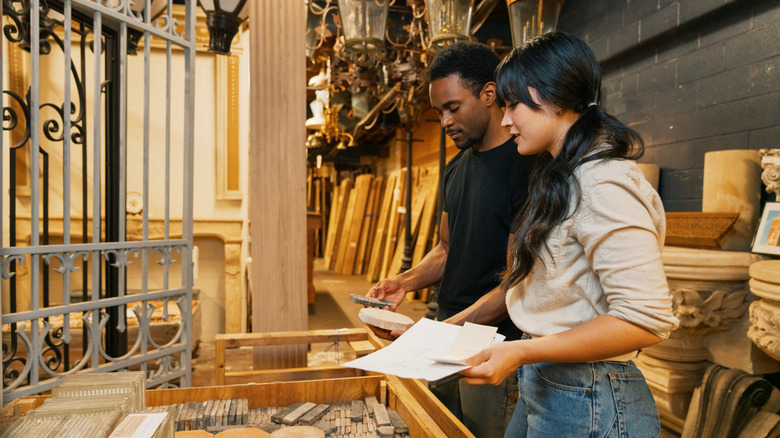 Two people shop for outdoor landscaping materials, including fencing materials, in a hardware store.
