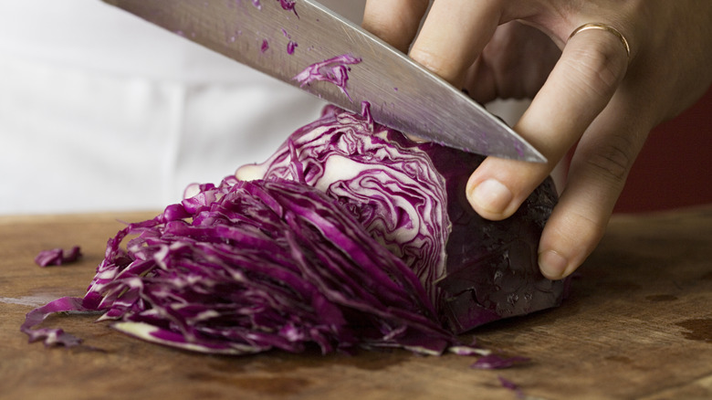A person uses a knife to slice a small red cabbage on a cutting board.