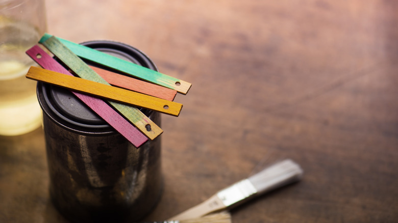 Five paint sticks colored with different wood stains sit on top of a tin can.