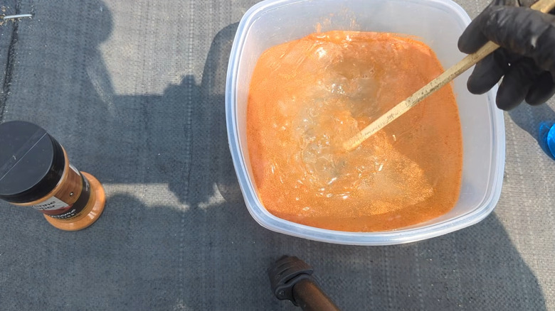 A person mixes cayenne pepper into water in a white plastic container to make a pest repellent spray for garden plants.