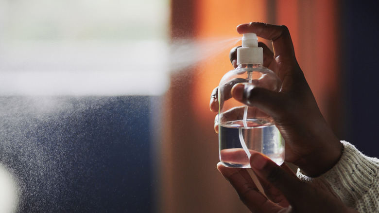 Woman's hand spritzing solution out of a clear spray bottle
