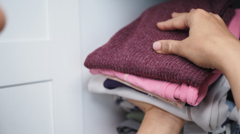 Person's hands putting folded clothes away in closet.