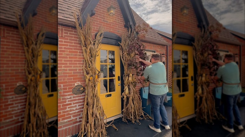 Man decorating his exterior doors with dried cornstalk bundles