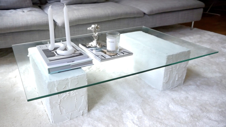 A coffee table made of concrete blocks covered in textured white plaster and a glass tabletop.