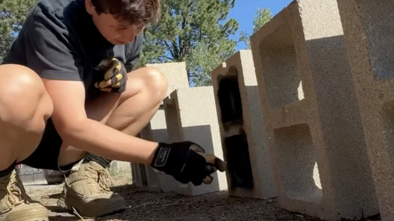 A person decorates concrete blocks with black spray paint.