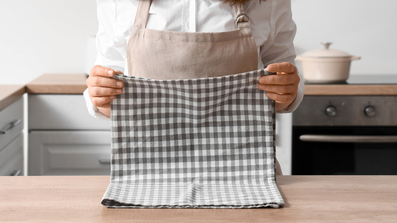 Woman folds a plaid kitchen towel on a wood countertop.