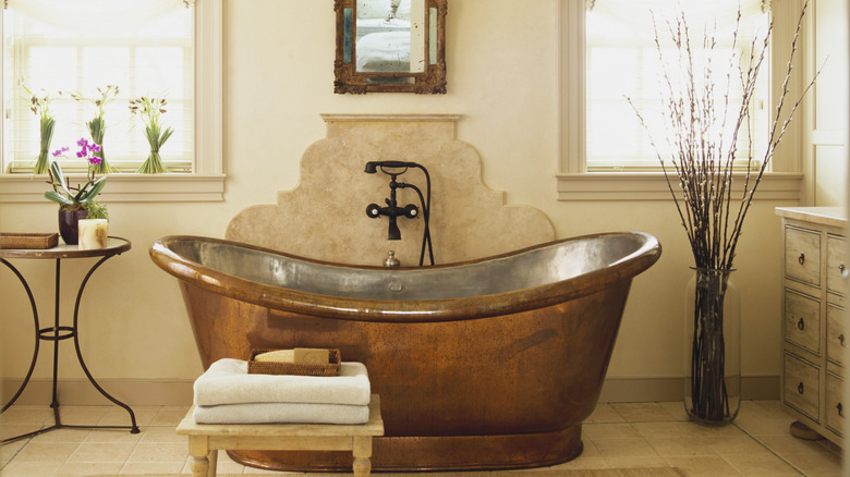 An old-world copper bathtub sits against a brightly-light beige wall.