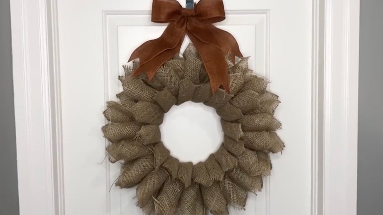 A rustic burlap wreath hanging on a white door.