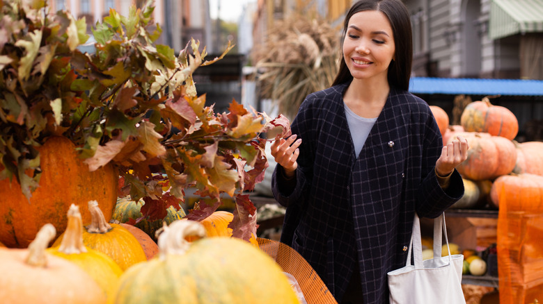 A person shopping for fall decorations at an outdoor market with pumpkins in the background