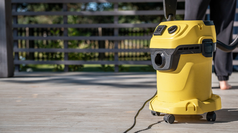 Yellow shop vacuum on a wooden deck near a fence