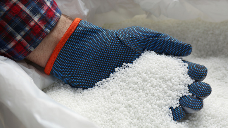 Gloved hand scooping urea pellets from fertilizer bag