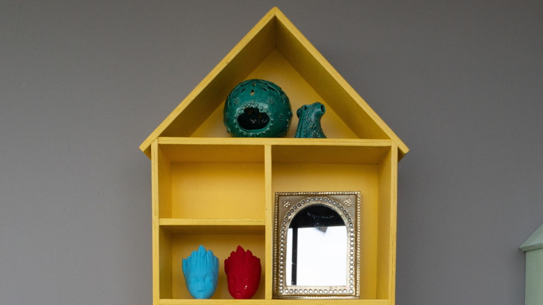 A yellow trinket house with a mirror and other trinkets in the spaces