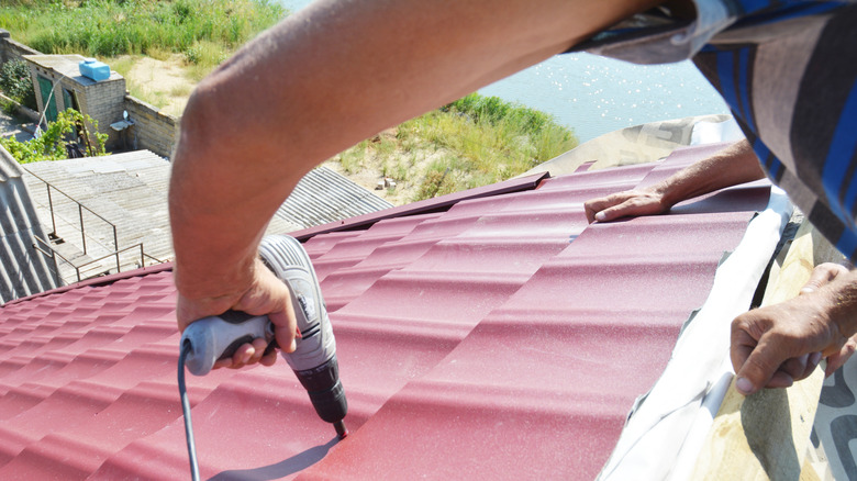 A person nailing down strips of red metal onto a roof