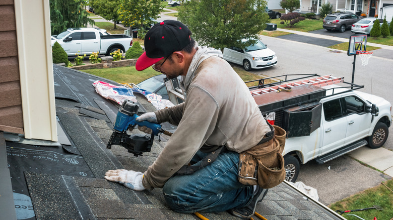 A man installing asphalt shingles on a roof with a nail gun