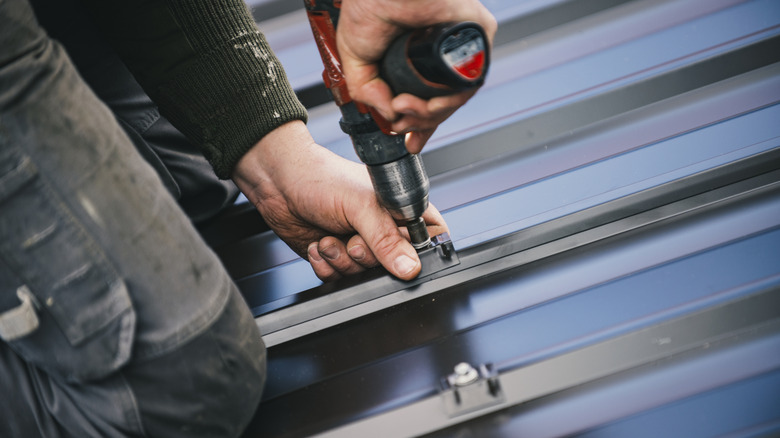 A person bolting down textured metal roof pieces