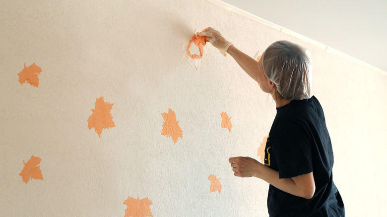 A woman in a hairnet painting leaves on a wall using stencils.