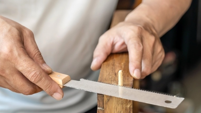 man using flush cut saw to cut wood dowel stuck into end of wood board