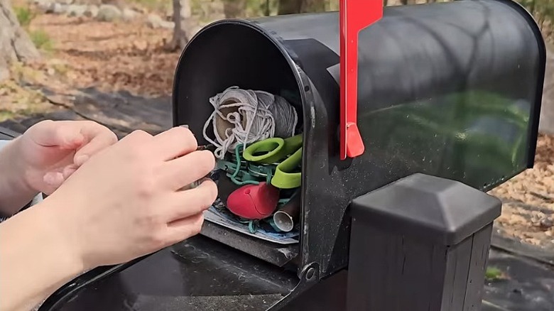 Hands reaching inside an extra mailbox used to tool storage in the garden