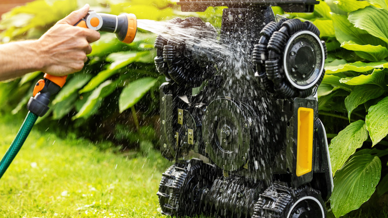 A person washing the deck of a lawn mower with a hose