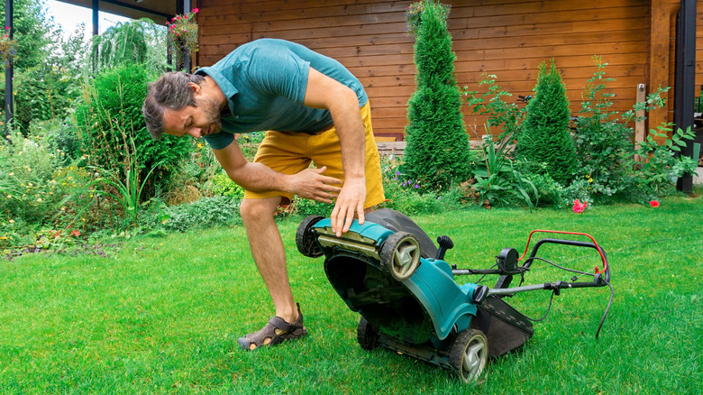 A man inspecting the underside of his lawn mower in a green yard