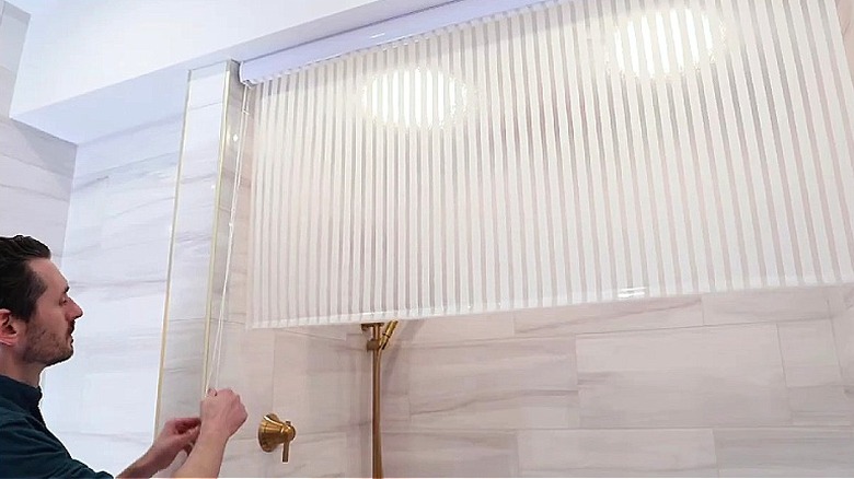 A person pulling the cord to roll up a Jakooz ceiling-mounted rollup shower curtain from Amazon