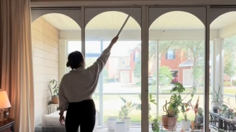 An influencer standing pointing to the cardboard arches on her sliding glass doors with a ruler.