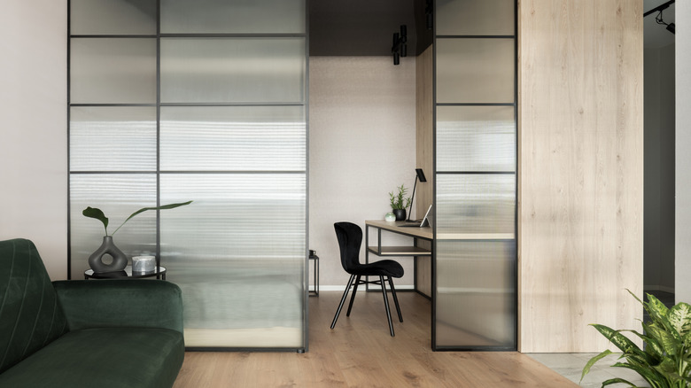 An office with a frosted sliding glass door that separates it from the open plan living room in a home.
