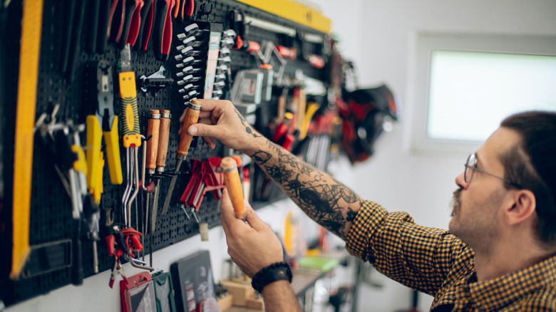 A man retrieving tools from a rack on a workshop wall