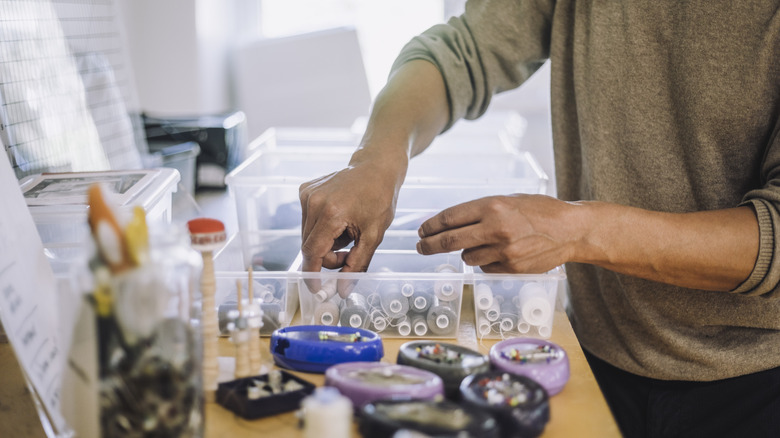 Person in taupe sweater organizing rolls of sewing thread into containers