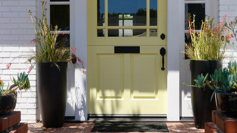Porch with yellow door and tall planters on either side