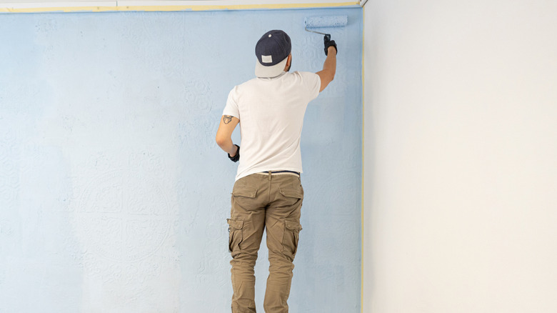 Man standing on stool and painting a wall light blue
