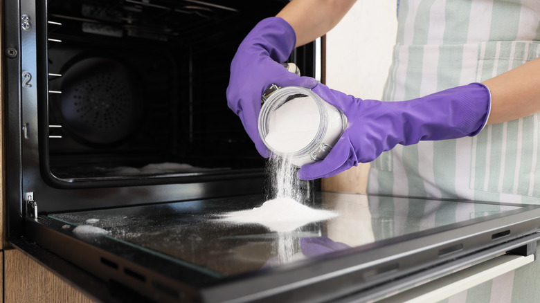 Woman in purple gloves pouring baking soda onto glass oven door