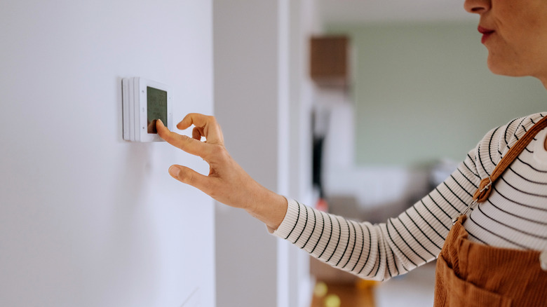 Person in a striped shirt and brown overalls touching a thermostat to adjust the settings