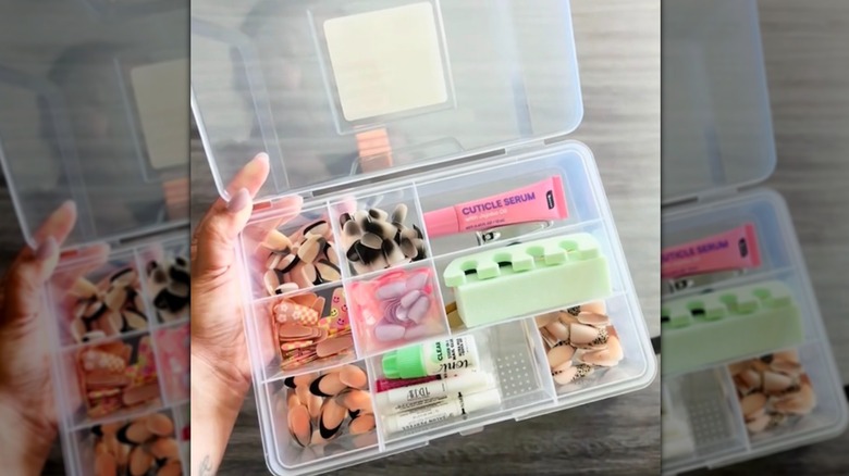 Woman's hand holding a plastic compartment case used as a nail kit.