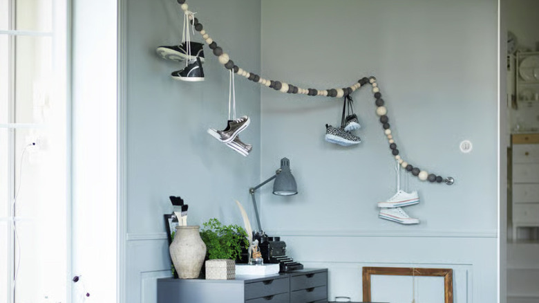 A curtain wire covered with wooden balls in the corner of a room with sneakers hung over it by their laces.