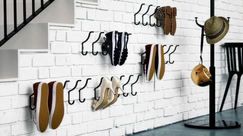 Hooks attached to a white painted brick wall with shoes hung off them, with a hat and bag stand next to them.